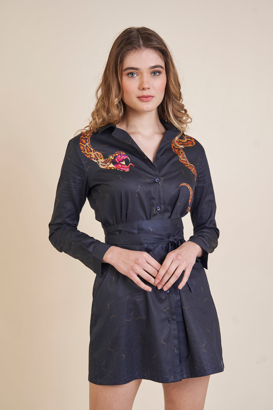 A woman wearing a snake print shirt dress, showing off the V-neckline, button-front design and belted waist
